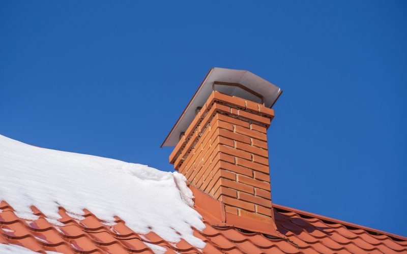 Red roof of a detached house and chimney and snow against the blue sky in winter, close up